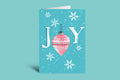 Christmas card with 'JOY' and a pink ornament on a teal background