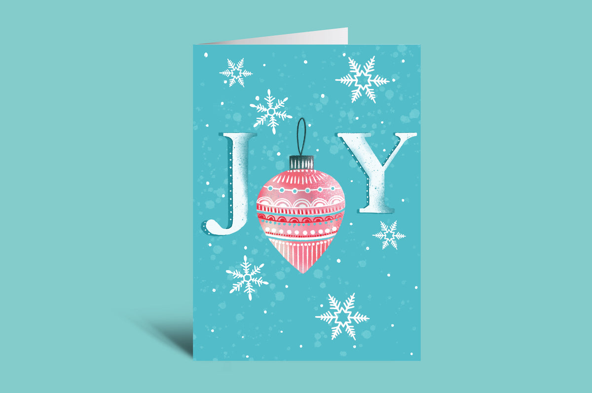 Christmas card with 'JOY' and a pink ornament on a teal background