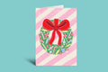Greeting card with a Christmas wreath and red bow on a striped background