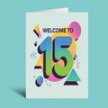 A folded greeting card standing upright on a light aqua background. The card has a white base and features a colorful 3D-style '15' with the words 'WELCOME TO' above it, surrounded by abstract geometric shapes in pink, yellow, green, blue, and purple.