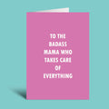 A pink greeting card with white text reading 'TO THE BADASS MAMA WHO TAKES CARE OF EVERYTHING' on a solid teal background.