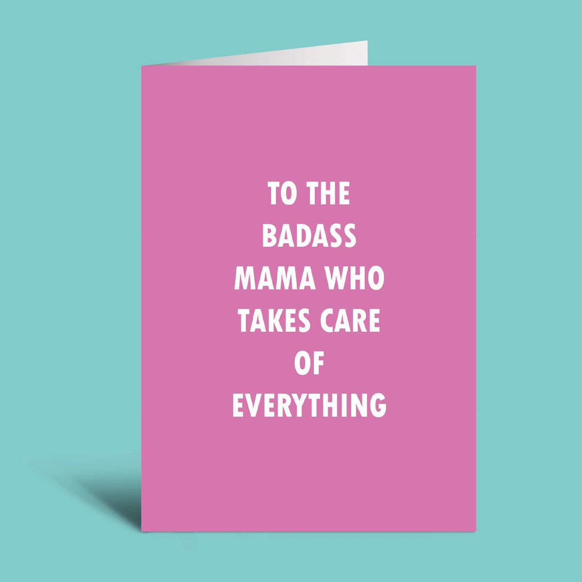 A pink greeting card with white text reading 'TO THE BADASS MAMA WHO TAKES CARE OF EVERYTHING' on a solid teal background.