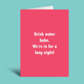 A pink greeting card with white text that reads 'Drink water babe. We're in for a long night!' shown standing against a light blue background.