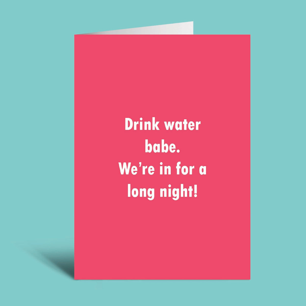 A pink greeting card with white text that reads 'Drink water babe. We're in for a long night!' shown standing against a light blue background.