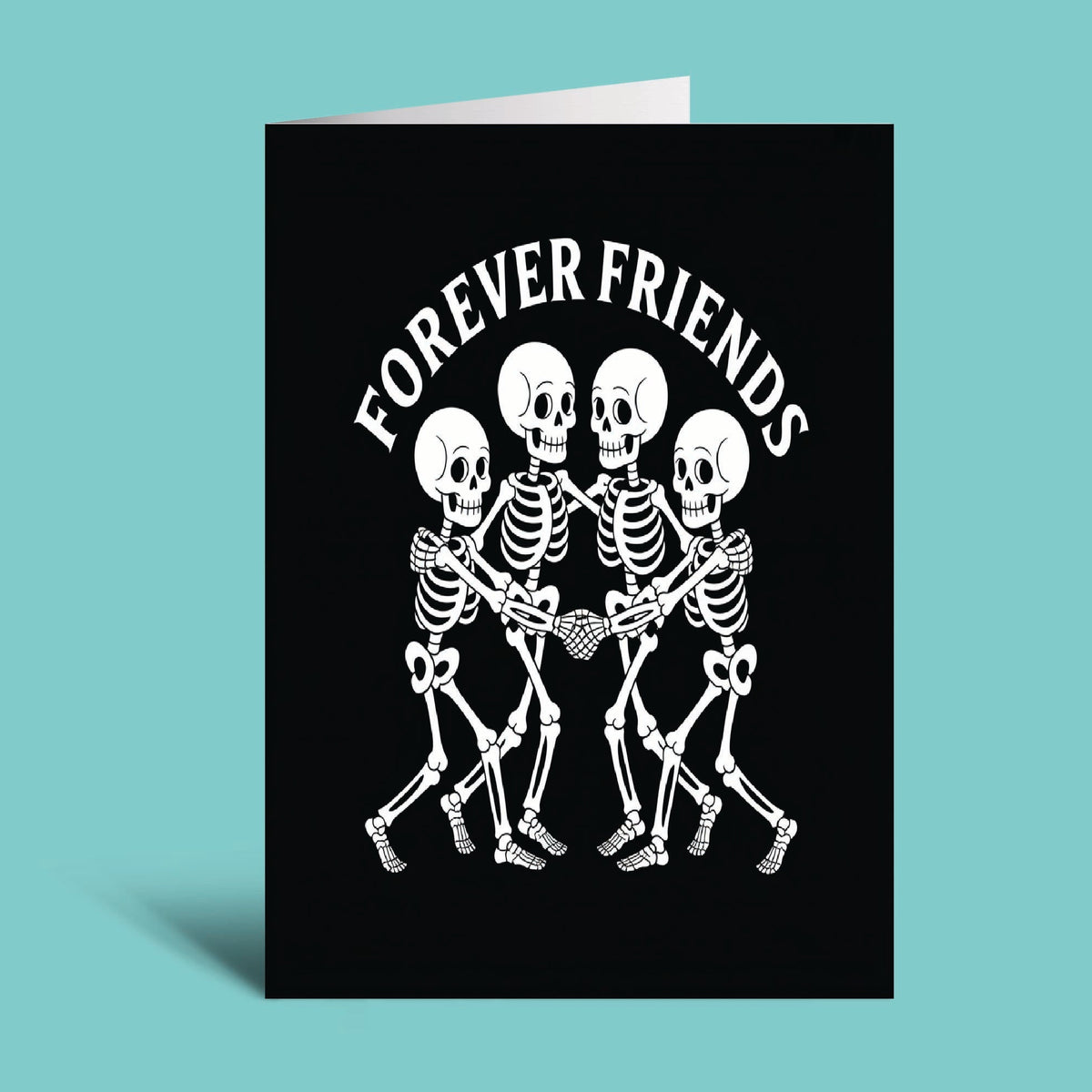 A black greeting card standing upright against a light aqua background, printed with the phrase 'FOREVER FRIENDS' above a white graphic of four skeletons holding hands.