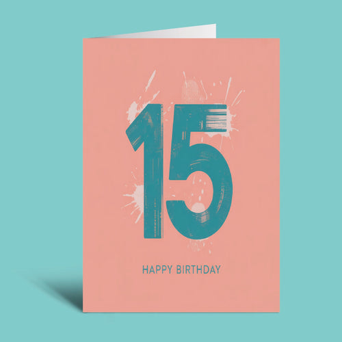 A coral pink 15th birthday greeting card with a teal '15' and white paint splatters, with 'HAPPY BIRTHDAY' printed below, shown on a solid teal background.