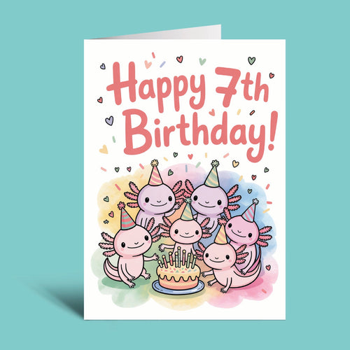 A folded greeting card standing upright on a light aqua background. The card has a white base with the text 'Happy 7th Birthday!' in coral pink lettering and a colorful illustration of five cute pink axolotl-like characters wearing party hats around a birthday cake.