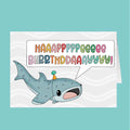 Birthday card with a cartoon shark and colorful 'Happy Birthday' text on a white background.