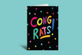 Greeting card with 'Congrats!' in colorful letters on a black background with polka dots, against a teal background.