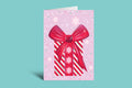 Greeting card with a candy cane and bow design on a light purple background with snowflake patterns, against a teal background.