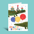 Birthday card with a crocodile holding balloons and the text 'Snappy Birthday' on a teal background.